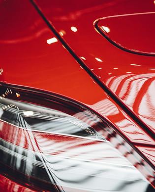 A glossy red vehicle finish reflecting bright inspection lights