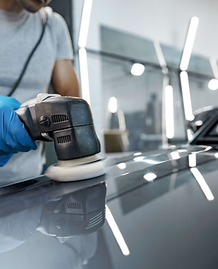 A detailer polishing a gray vehicle panel under inspection lighting